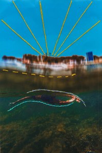 Fotografia vertical de uma paisagem com interferências digitais, como borrado, e manuais, como pespontos e alinhavos. Em primeiro plano, uma pessoa nada para a esquerda em águas esverdeadas sobre corais verde-escuros. Os pés estão próximos à superfície, ligeiramente curvos e iluminados. O corpo, visto parcialmente, é alongado.O braço esquerdo está esticado para o lado com a mão aberta. Contornando o corpo, acima, um alinhavo com linha espessa roxa, espiralada de amarelo; e, abaixo, com linha azul, também espiralada de amarelo. Acima, um pesponto amarelo parece flutuar nas águas um pouco borradas que refletem a luz da margem de uma cidade manchada com topo marrom e base intensamente iluminada. À direita, um edifício azulado. Sobre o céu azul, seis raios de linhas amarelas despontam do centro da cidade até a margem superior.